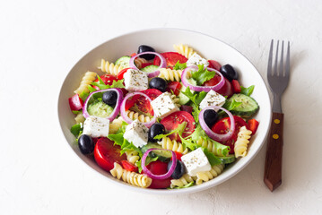 Greek pasta salad with feta cheese, tomatoes, onion, cucumbers, peppers and olives. Healthy eating. Vegetarian food.