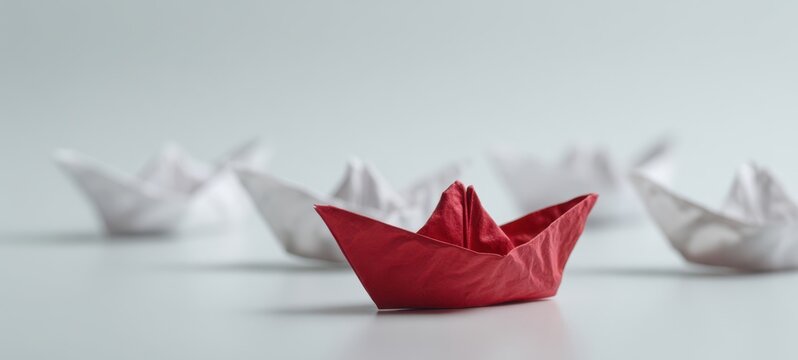 The red paper boat standing out among white paper boats on soft background