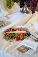 Plate with assorted cured meats, herbs and breadsticks on elegant white banquet table.