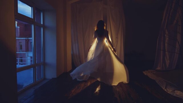 Dark shadow silhouette young sexy woman in long silk peignoir runs to warm light canopy bed curtains white fabric fly in wind windows bedroom night black room. girl bride in dress robe back rear view.