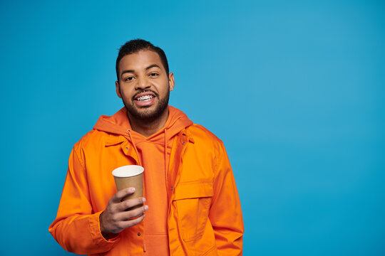 Young african american man enjoys a drink while dressed in vibrant orange casual attire