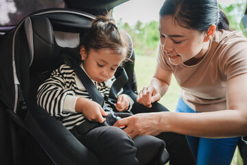 mother is fastening safety belt to toddler girl in car seat, safety baby chair travelling