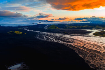 Aerial view of Iceland's volcanic landscape at sunset, featuring black terrain, glacial rivers, a...