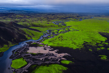Aerial view of green moss covered land with dark volcanic soil, meandering rivers, and distant...