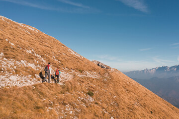 Fototapeta premium Mountaineer couple with backpacks and trekking poles doing a high mountain route on a nice sunny day. Seasonal vacation concept.