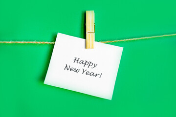greeting card for the annual holiday Christmas and New Year green background and white paper with the inscription Happy New Year, with space for text, the card hangs on a rope and is held on a clothes