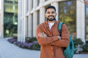 Smiling young man with backpack standing in front of modern building