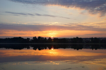 Beautiful moments of sunrise. Shot from the surface of the lake, the shore and trees against the beautiful sky. Morning fog. Reflection on the surface of the water.
