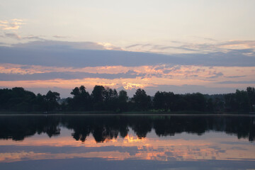 Beautiful moments of sunrise. Shot from the surface of the lake, the shore and trees against the beautiful sky. Morning fog. Reflection on the surface of the water.