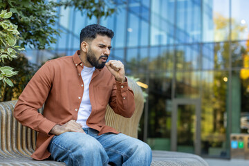 Sick man coughing on a bench in the city