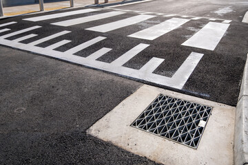 Raised pedestrian crosswalk on an asphalt road with stormwater drain. Designed for safer crossing...