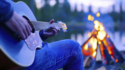Obraz premium Person plays acoustic guitar by campfire near lake, creating serene and cozy atmosphere. warm glow of fire contrasts with cool