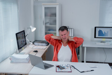 Businessman experiencing neck pain and discomfort while working on his laptop, highlighting the physical strain and health challenges associated with prolonged office work