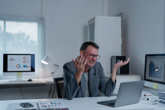 Stressed mature businessman getting angry and frustrated while working with laptop computer in office, he is having problems with online meeting, data analysis or project failure
