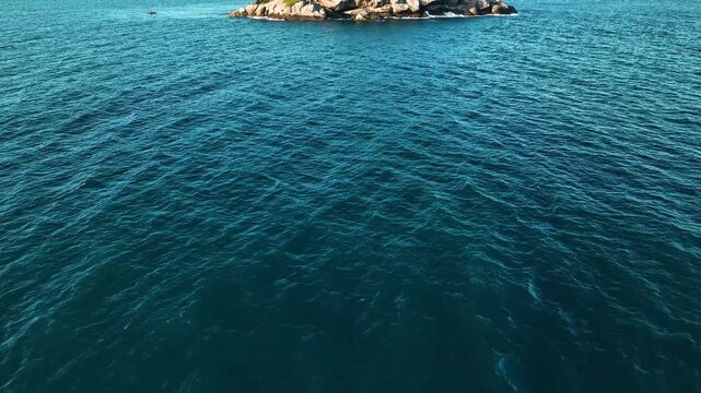 Aerial view of a rugged, rocky island with sparse green vegetation surrounded by the deep blue ocean waters, Paraty, State of Rio de Janeiro, Brazil.