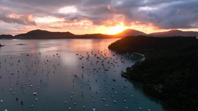 Aerial view of numerous white boats scattered across the tranquil waters at sunset, creating a stunning contrast against the dark green coastline, Paraty, State of Rio de Janeiro, Brazil.