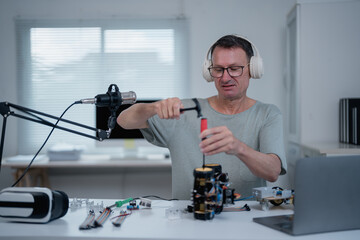 Electronics engineer wearing headphones assembling robot while recording podcast for his online audience using professional microphone in his modern bright office