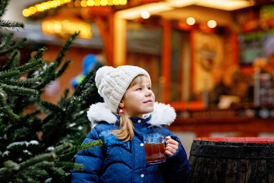 Little cute preschool girl drinking hot children punch or chocolate on German Christmas market. Happy child on traditional family market in Germany, Laughing boy in colorful winter clothes