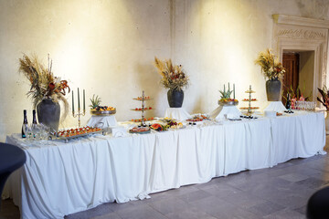 Long decorated buffet table with drinks, fruit, appetizers, and flowers for celebration.