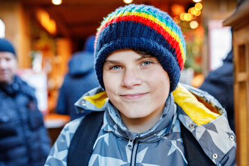Teenage boy having fun on traditional Christmas market during strong snowfall. Happy teenager child enjoying traditional family market in Germany