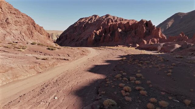 Aerial view of a car driving through the stunning Valle del Arcoiris, its white paint contrasting with the arid, red-rock landscape, San Pedro de Atacama, Chile.