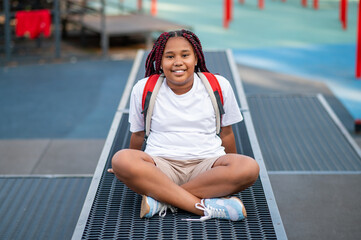 Smiling teen girl sitting with her legs crossed and looking contented