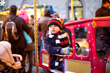 Funny little kid boy on a carousel at Christmas funfair or market, outdoors. Happy child having fun. Traditional xmas market in Germany, Europe. Holiday, children, lifestyle concept.. © Irina Schmidt