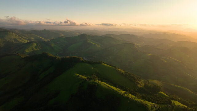 Aerial view of rolling green hills bathed in the golden light of dawn, contrasting with the deep shadows in the valleys, Monte Verde, State of Minas Gerais, Brazil.