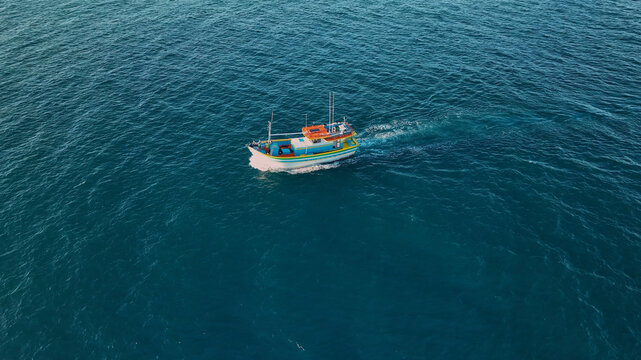 Aerial view of a vibrant fishing boat slicing through the deep blue sea, its wake a frothy contrast, Paraty, State of Rio de Janeiro, Brazil.