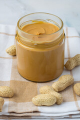 Jar of peanut butter and raw peanuts in shells on light background