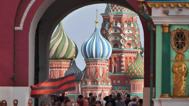 Saint Basil's Cathedral framed by Resurrection Gate with waving Ribbon of Saint George in Moscow.