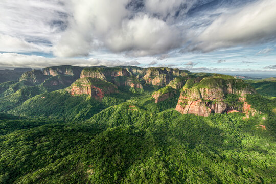 Fototapeta Aerial view of vibrant green jungle contrasting with red rock formations under a dynamic sky in Amboro National Park, Samaipata, Bolivia.