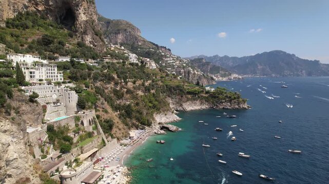 Stunning drone footage capturing the coastal beauty of Conca dei Marini in Amalfi, with cliffs, boats, turquoise sea, and luxury villas on a sunny day.