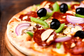 Pizza with chorizo ​​sausage, mozzarella cheese, green pepper and black olives. Rustic wooden background. Soft focus.	