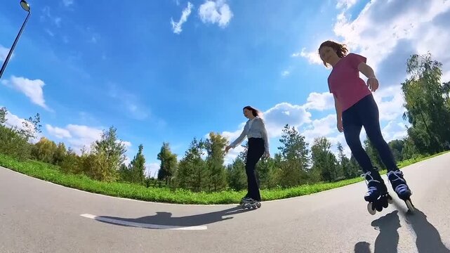 Two Caucasian women roller skating in a park. 