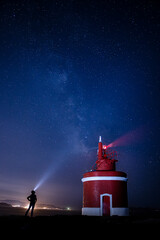 A Night Watcher and the Red Lighthouse Under a Starry Sky. The Milky Way is visible overhead,...