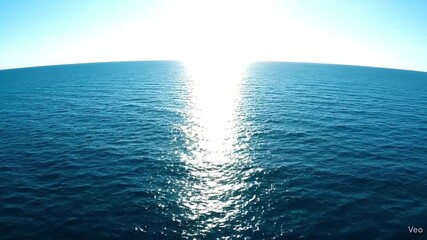 Blue ocean under a sunny sky with bright light reflecting on the waters surface and horizon visible