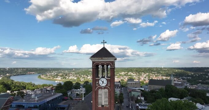 Cincinnati, United States - 26 August 2025: Aerial view of a clock tower amidst buildings along a curving river under a sky dotted with fluffy clouds.