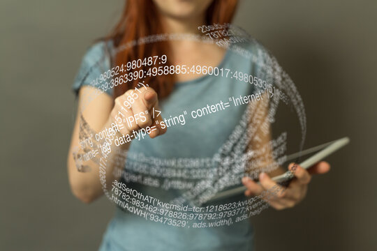 A woman uses a tablet to interact with a holographic display of code.