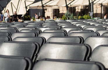 Empty black plastic chairs for a concert, wedding or business conference stand in rows in the town square  Folding chairs stand in a row for a public event in the city