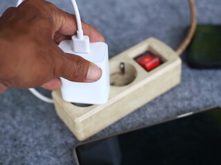 Close up of a person's hand holding a charging adapter to charge a cell phone.
