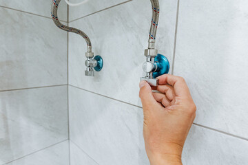 This closeup shot highlights a hand turning a water shutoff valve in a modern shower, showcasing...