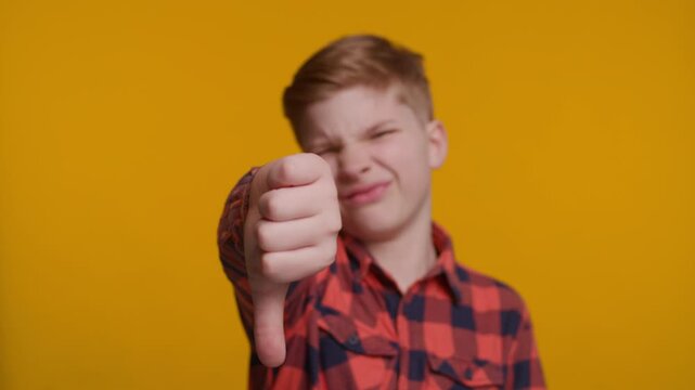 Boy Shows Thumbs Down at Camera on Yellow Background