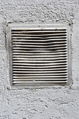 A dusty, weathered white vent is set into a gray, textured wall, showing signs of wear and tear