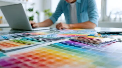 Professional graphic designer working on laptop surrounded by colorful pantone swatches and design materials in bright creative workspace studio environment © Ruslan Gilmanshin