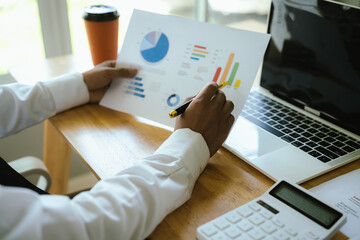 A businessman analyzes financial charts with a pen at the office desk, reviewing reports, data, and strategies for corporate success.