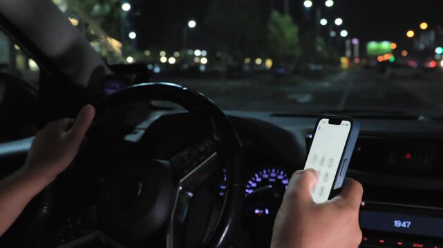 Driver using smartphone while driving car at night in city street traffic