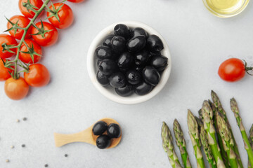Bowl of black olives with tomatoes asparagus and cooking ingredients
