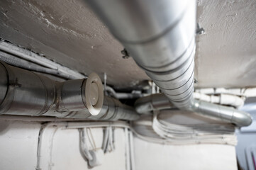 Metal ventilation pipes run across ceiling of basement. Scene shows engineering system for air circulation in private house