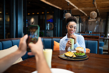 Diverse couple on a foodie date enjoys casual dining and a phone moment, sharing sunny vibes, drinks